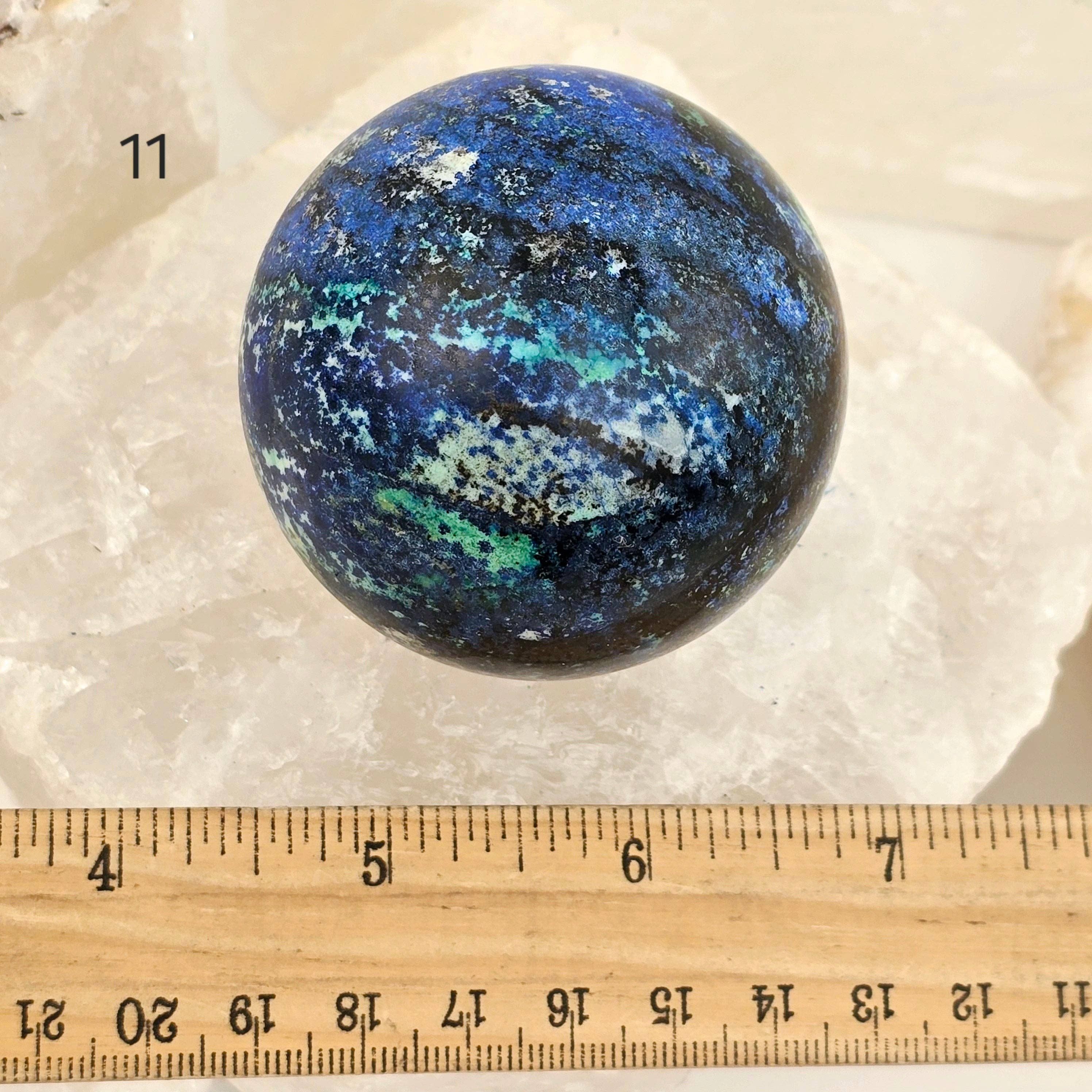 Blue and black marbled sphere on a white background with a ruler for scale.