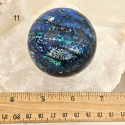 Blue and black marbled sphere on a white background with a ruler for scale.