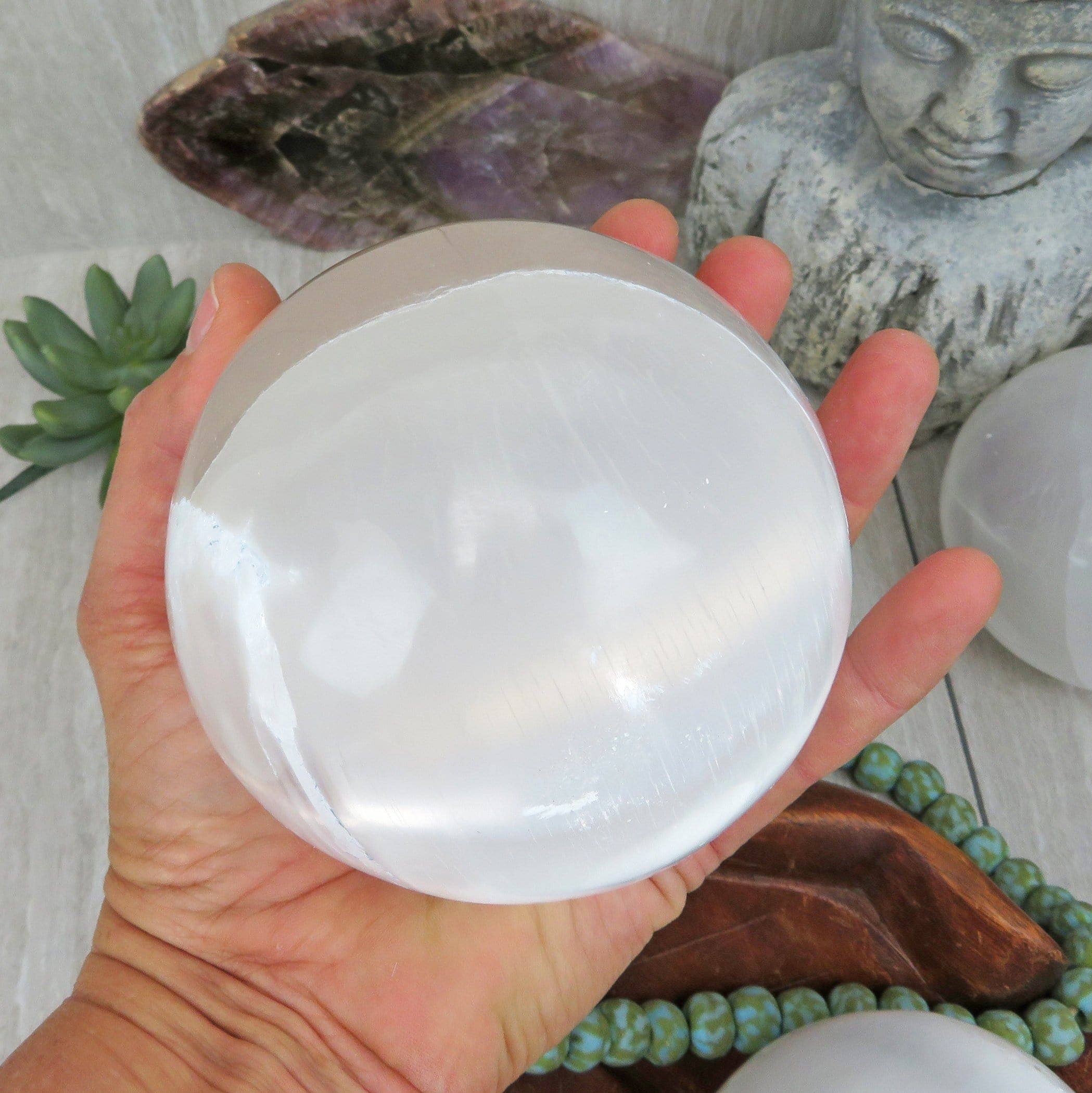 Hand holding a clear crystal ball with a blurred background of stones and plants