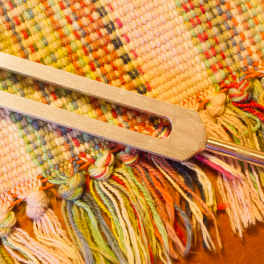 Close-up of a wooden knitting needle on a colorful knitted fabric.