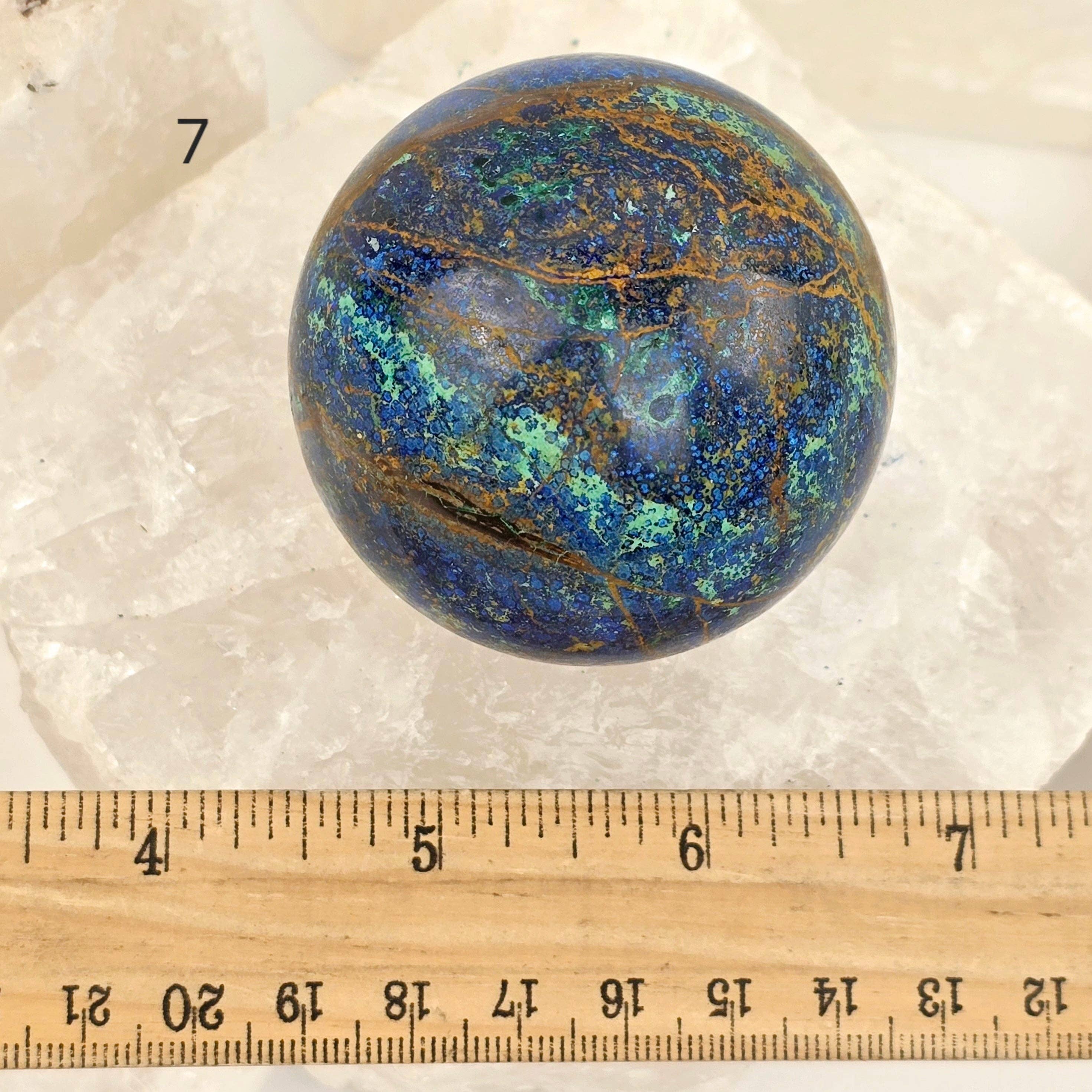 Marbled blue and green stone sphere on a white background with a ruler for scale.