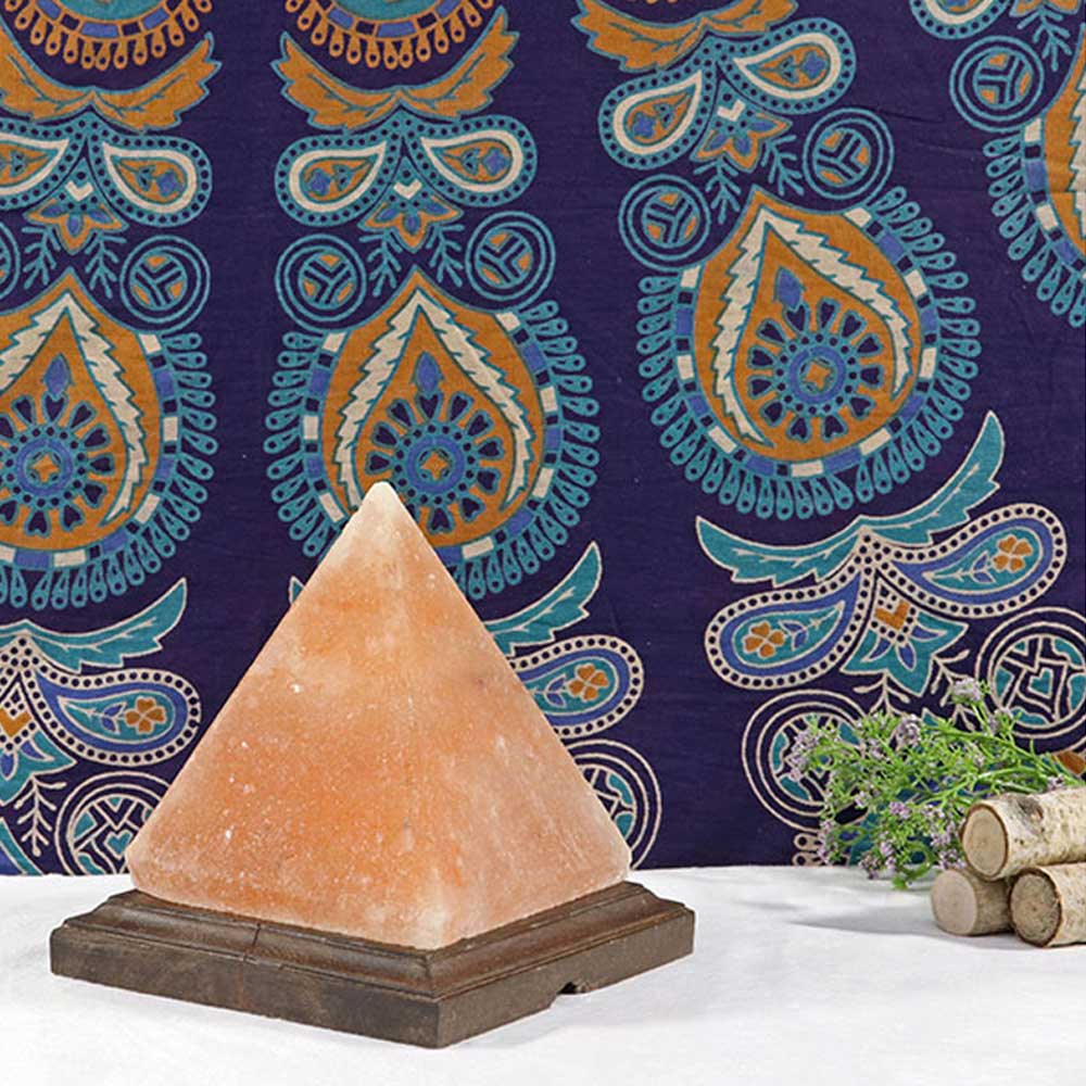 Pyramid-shaped salt lamp on a wooden base with a colorful paisley-patterned fabric in the background.