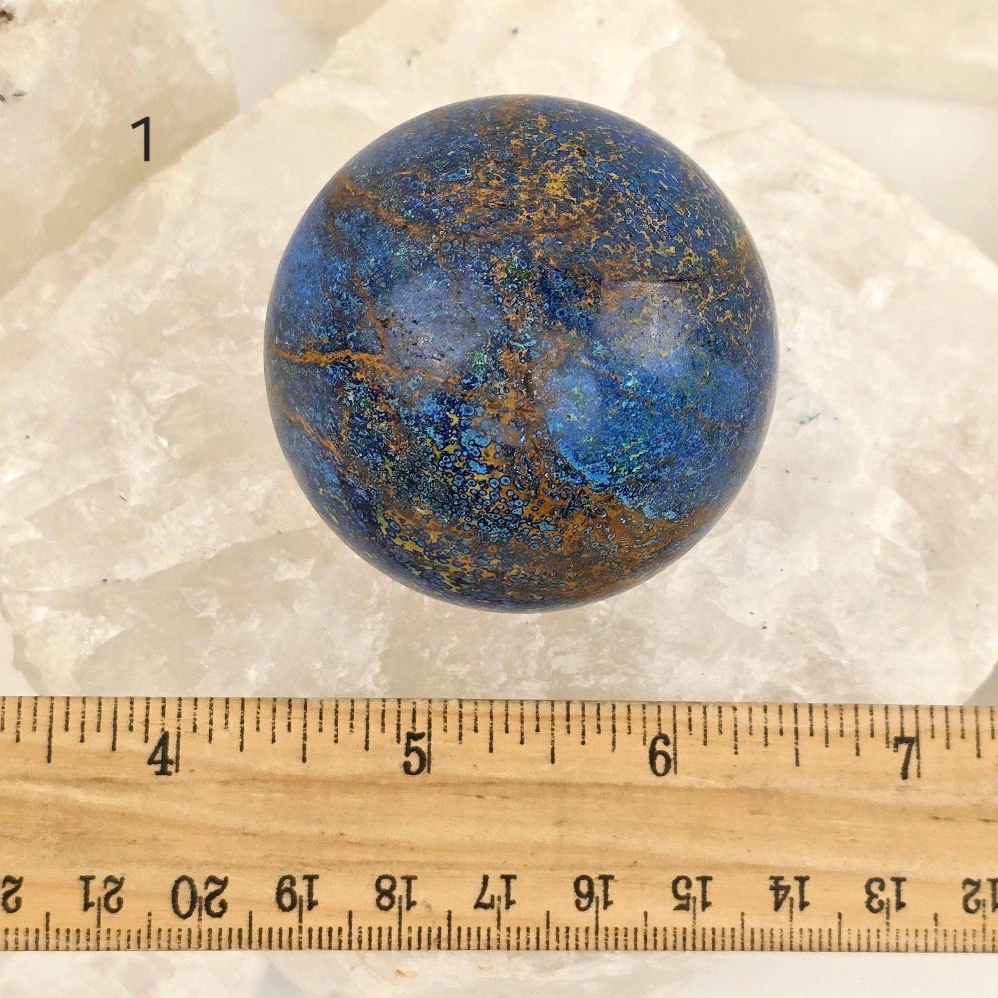 Blue and brown marbled stone sphere on a white background with a ruler for scale.
