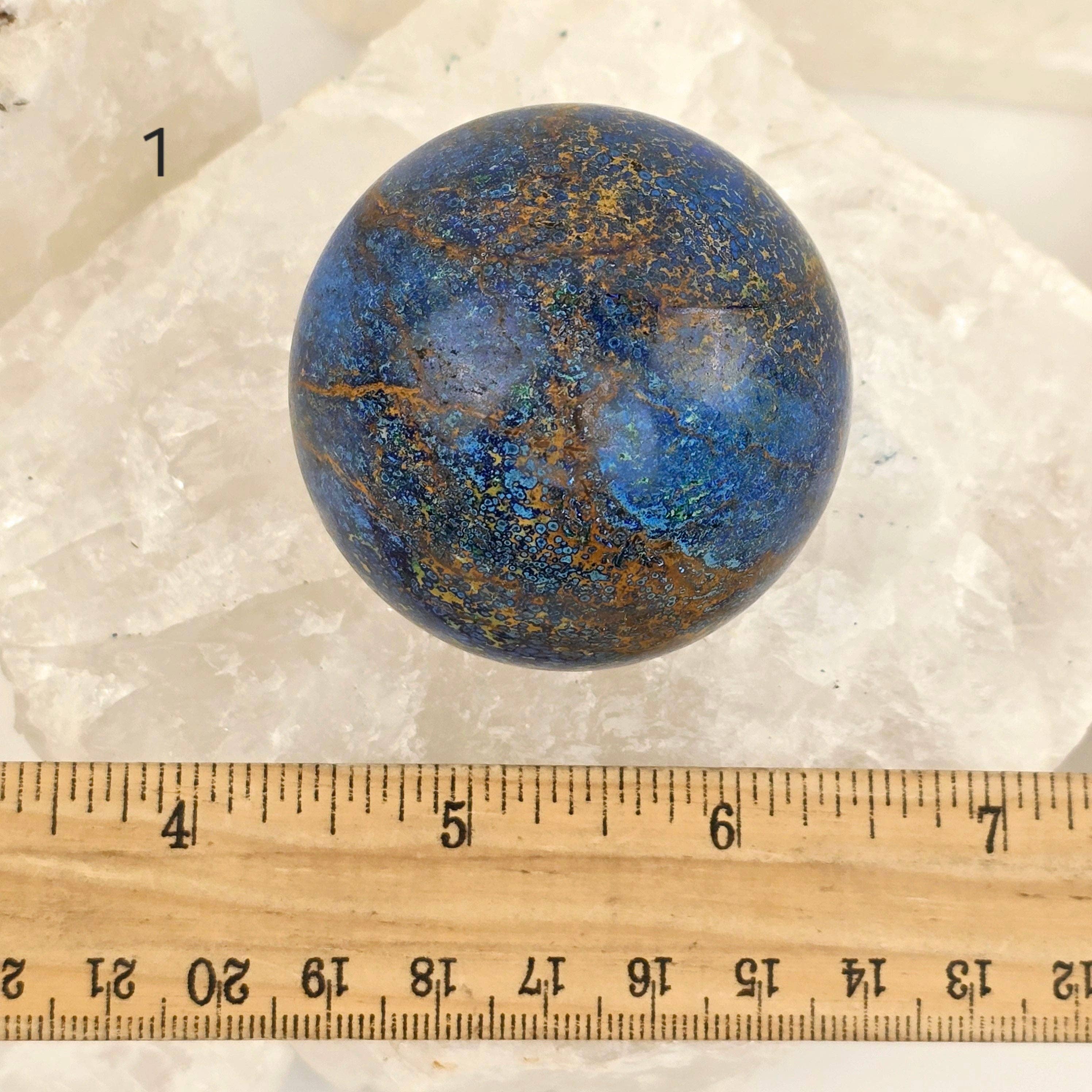 Blue and brown marbled stone sphere on a white background with a ruler for scale.