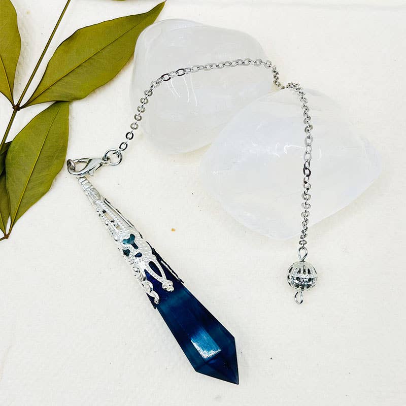 Necklace with blue crystal pendant on a white surface with green leaves
