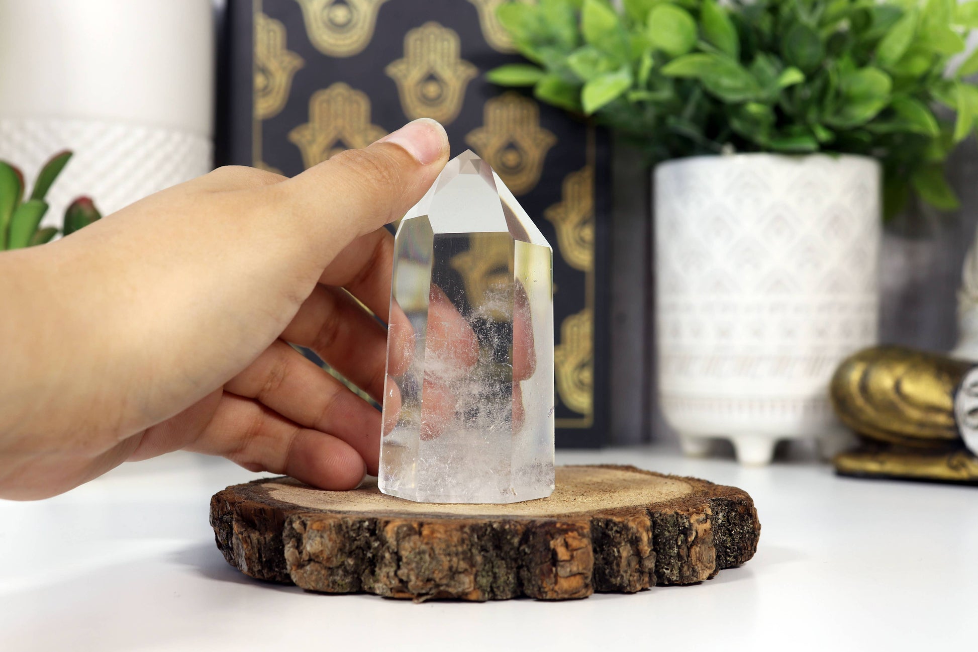 Clear crystal on a wooden stand with a hand holding it, against a background of decorative items.