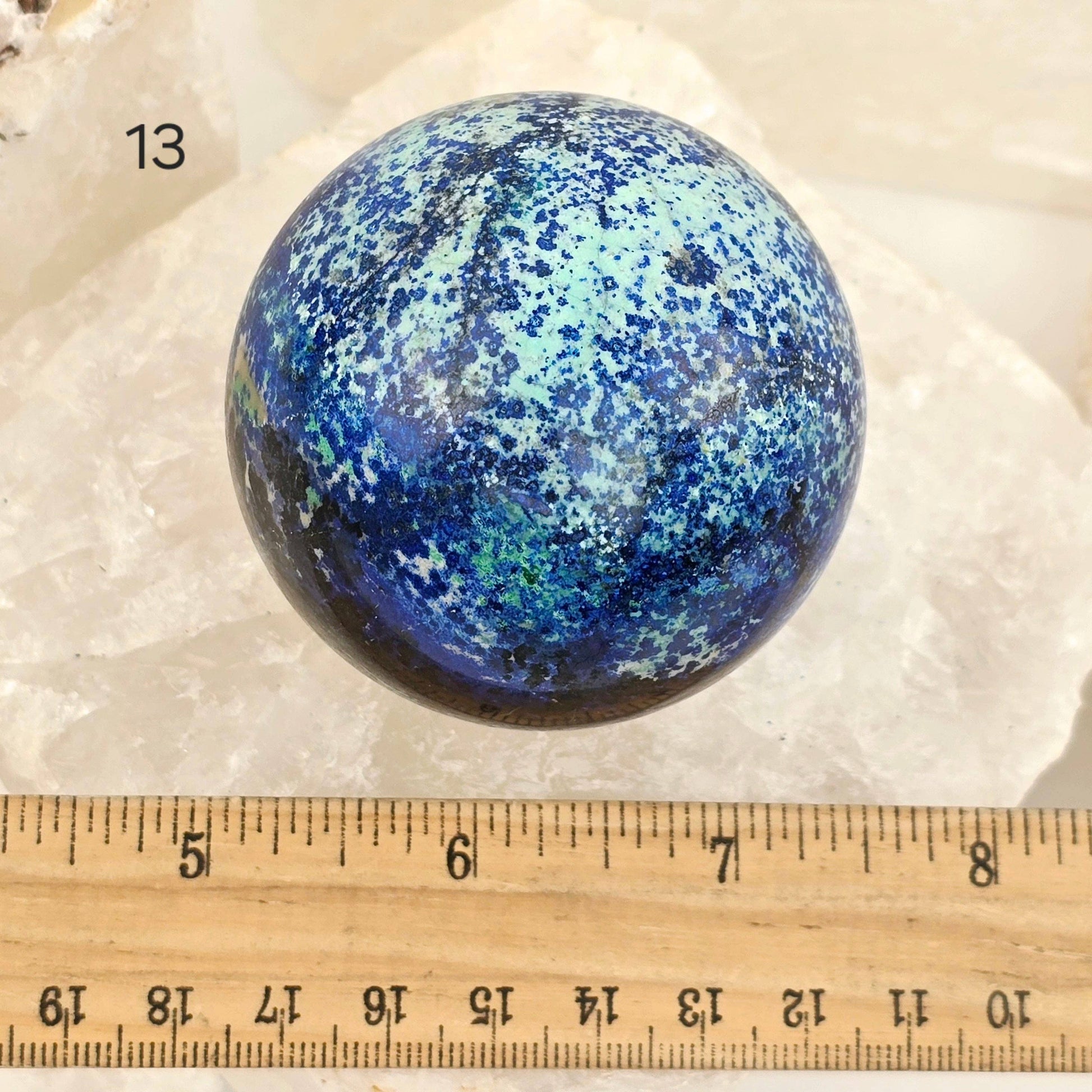 Blue speckled sphere on a white background with a ruler for scale.