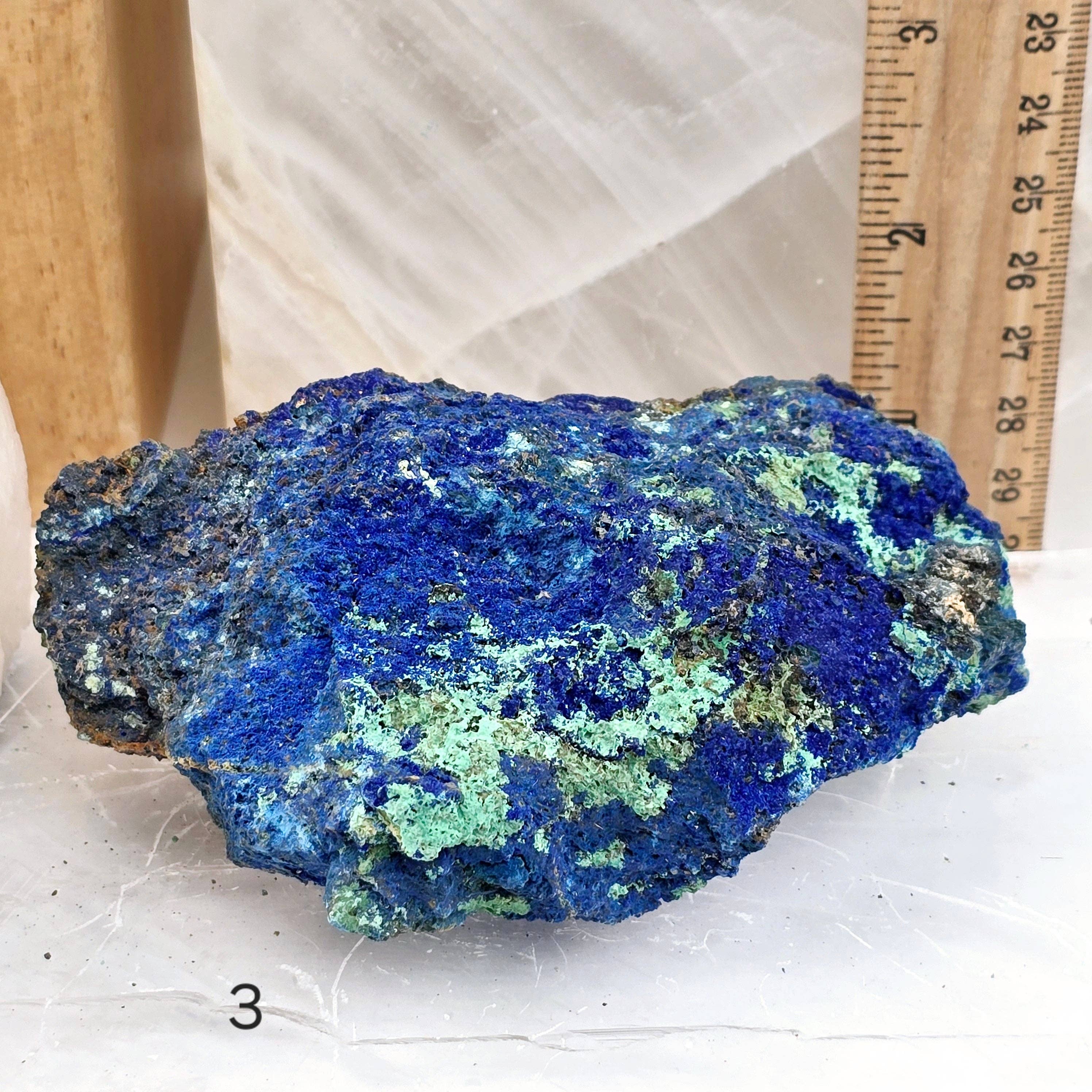 Blue and green mineral specimen on a white surface with a ruler for scale.