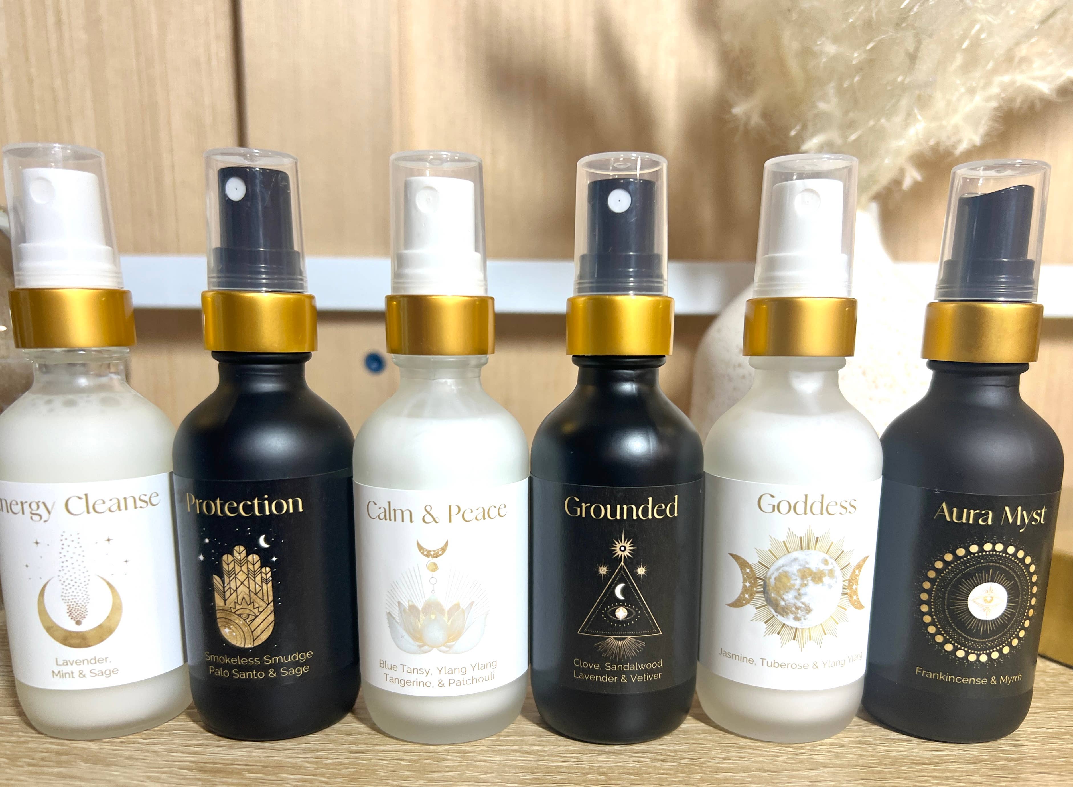 Set of six spray bottles with various labels on a wooden surface.