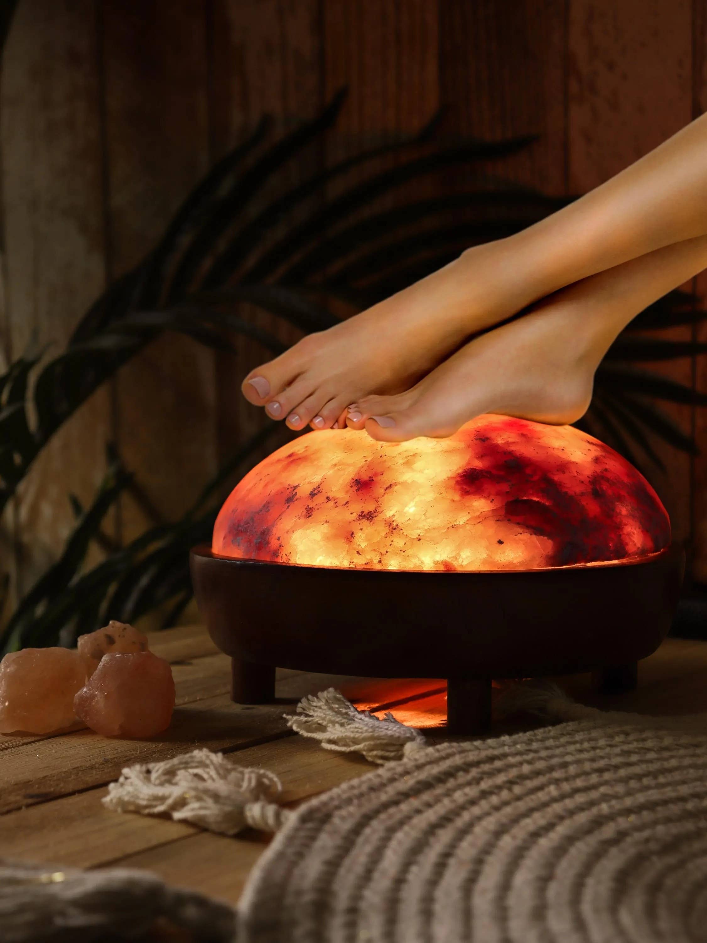 Feet being placed into a glowing red Himalayan salt lamp on a wooden surface.