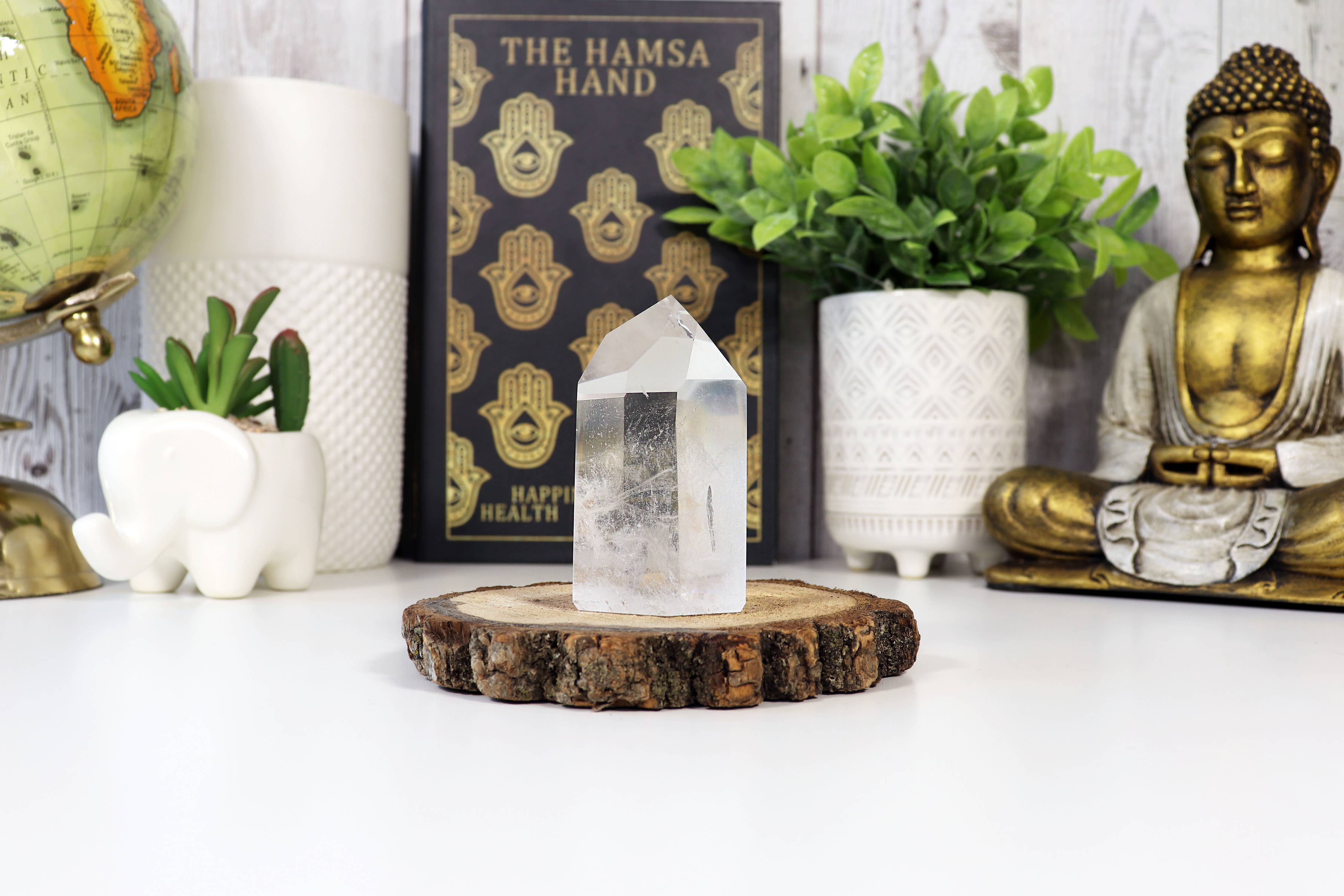 Crystal on a wooden stand with a Buddha statue, plants, and decorative items in the background.