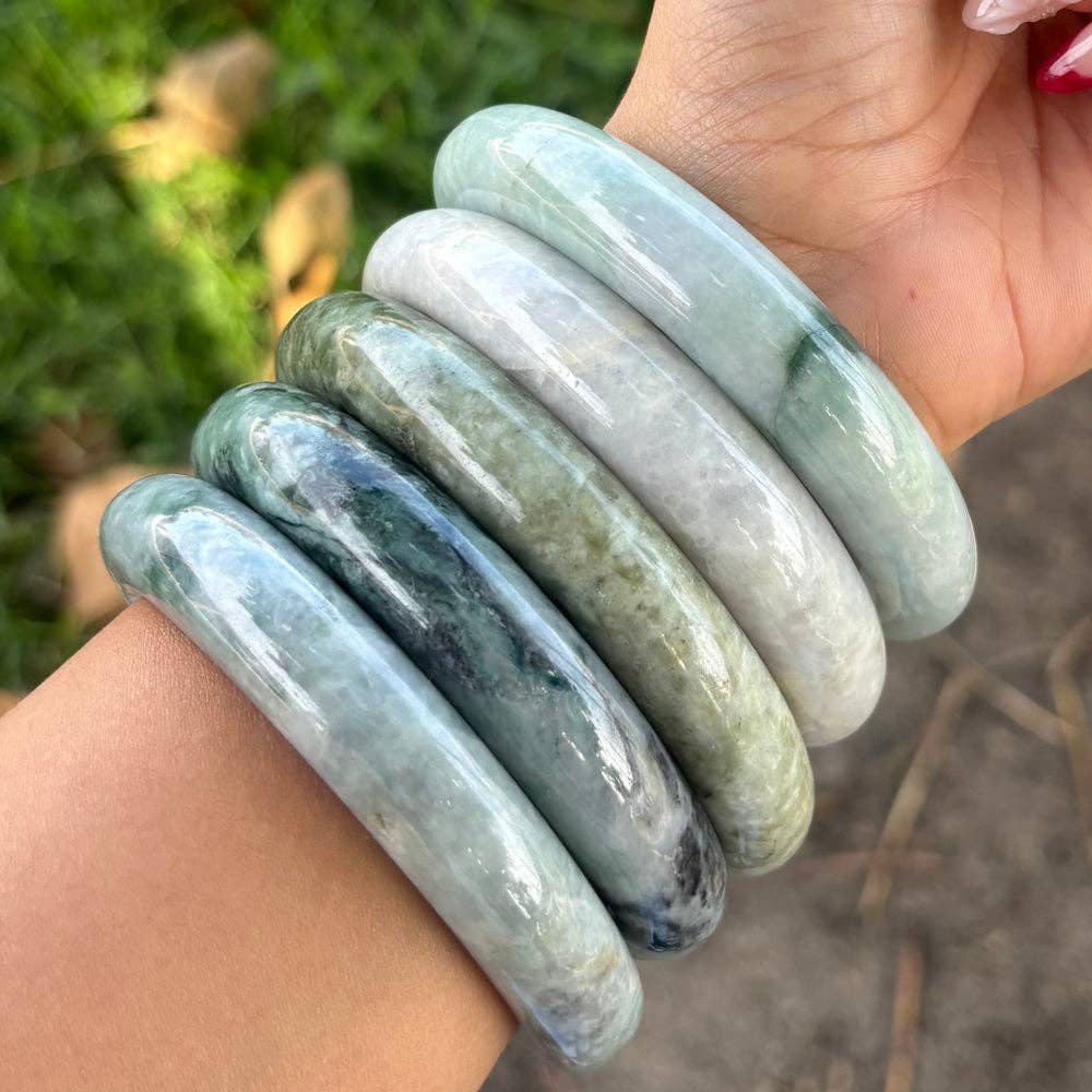 Hand wearing three green and white bangles with a natural outdoor background