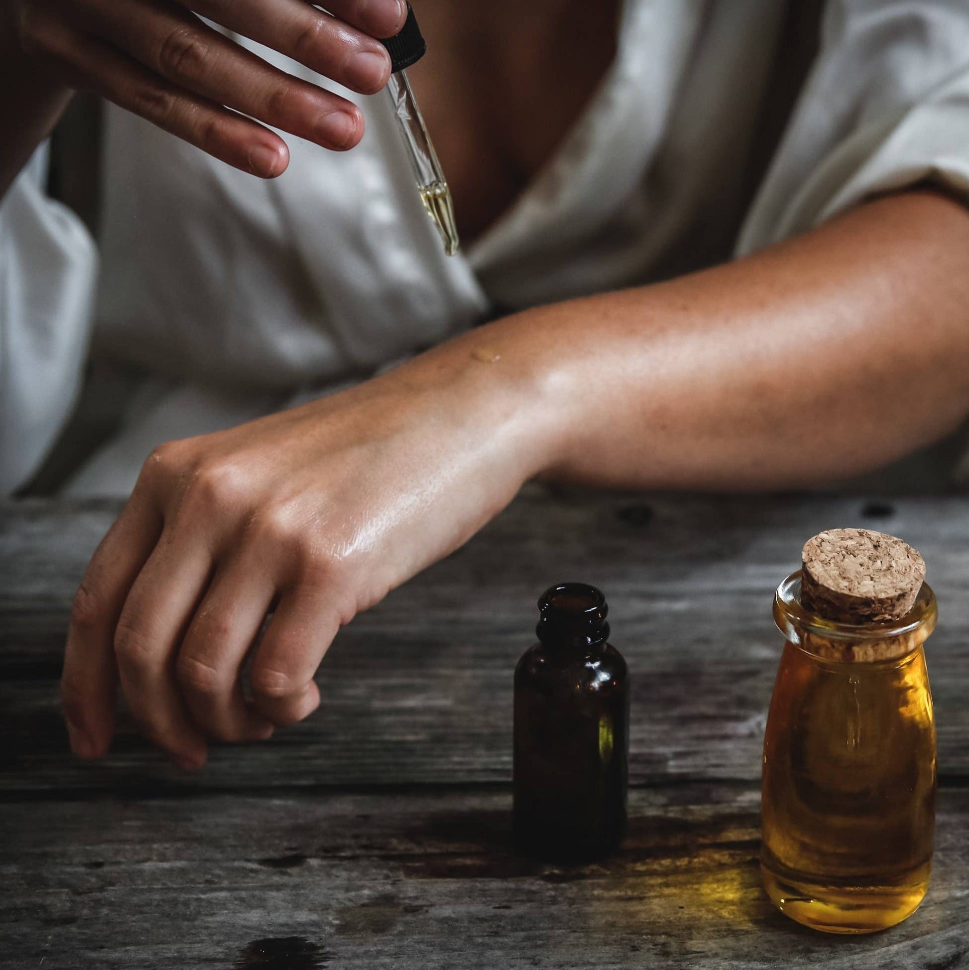 Person using a dropper to add liquid to an amber bottle on a wooden surface - JOY - Journey Of You - Spiritual, Holistic, Empowering