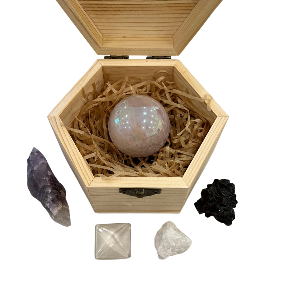 A Ascension Stone Kit displayed inside an open wooden box, including a sphere, a pyramid, and a crystal point, with a small amount of straw bedding. 